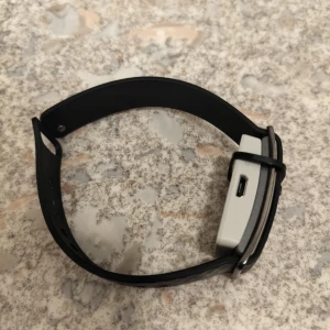 Svart aktivitetsklocka med rektangulär display - Säljer en svart aktivitetsklocka med rektangulär display och silikonarmband. Klockan har en USB-port på sidan för laddning. Perfekt för dig som vill hålla koll på din aktivitet och hälsa. Passar vanligt usb kabel 