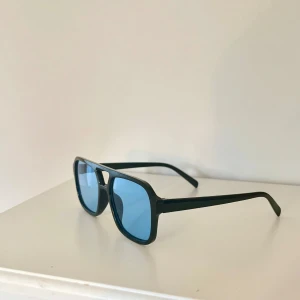 Svarta solglasögon med blåa glas - Snygga solglasögon med svart båge och rektangulär form. Glasen är blåtonade och ger en cool retrovibe🤵🏼Perfekta för att sticka ut i sommarens soliga dagar☀️