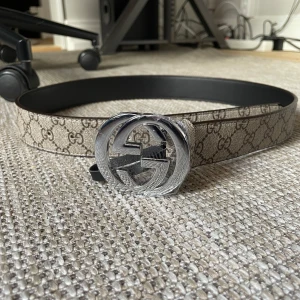 Gucci GG Supreme bälte med silverfärgat spänne - Säljer ett Gucci GG Supreme bälte med klassiskt monogrammönster och stort silverfärgat GG-spänne. Bältet är beige med bruna detaljer och har präglad märkning på insidan. Kommer med originalpåse och förpackning. Skriv för mer info eller frågor👌