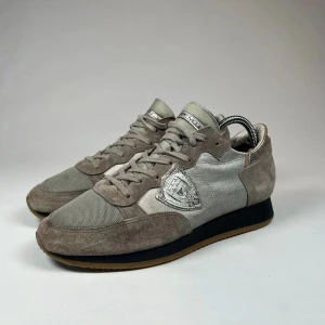 Grå sneakers från Philippe Model - Snygga grå sneakers från Philippe Model med en kombination av mocka och syntetmaterial. Skorna har en rund tå och snörning framtill. Perfekta för en stilren och bekväm look. Ny pris 3600kr