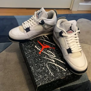 Vita sneakers från Nike - Snygga vita Nike sneakers med blå detaljer och snörning. Skorna har en rund tå och är perfekta för en sportig look. De kommer i en stilren design med märkets ikoniska logga på tungan och hälen.