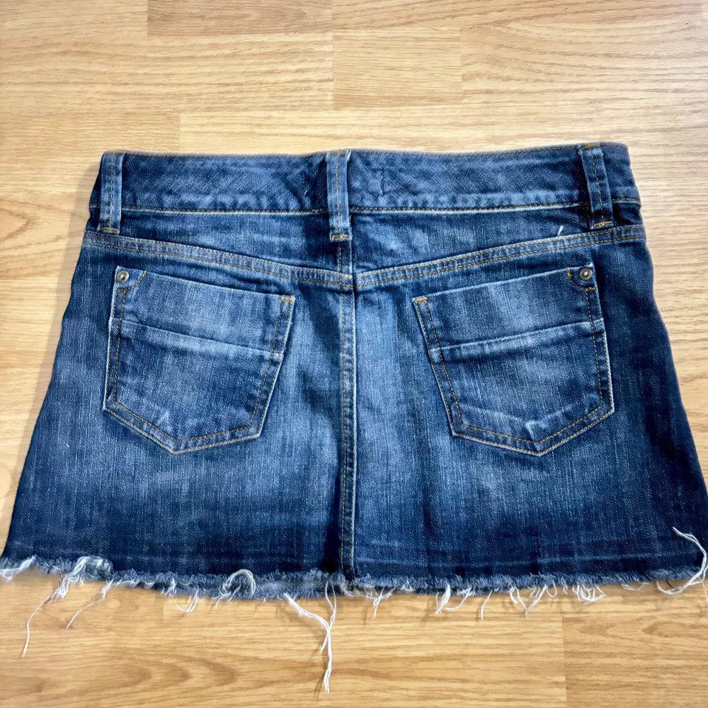 Snygg jeanskjol från Yeans Please i klassisk blå denim. Kjolen har en kort längd med fransig nederkant och femficksdesign. Perfekt för en avslappnad stil.. Hameet.