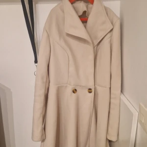 kappa med knappar - Elegant beige kappa med långa ärmar och stilrena knappar framtill. Perfekt för kyligare dagar med sin klassiska design och mjuka material. Nästan aldrig använt förutom fåtal gånger.