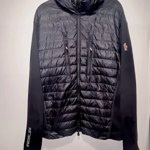 Moncler Jacka - Moncler jacka med vadderad polyester som håller värmen när det blir kyligare & ribbstickade partier i jungfru-ull. Storlek XL, men tack vare det stretchiga materialet passar den allt från M till XL beroende på önskad passform..
