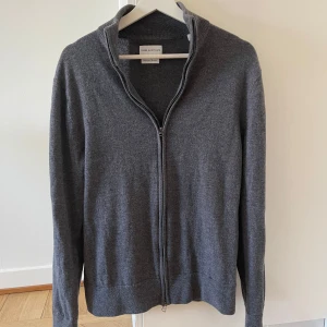 Merinoullskofta från These Glory Days - Säljer en stilren grå kofta i merinoull från These Glory Days. Köpt second hand. Storleken är L men skulle säga att den sitter mer som en M. OBS: Den har ett litet hål vid vänster axel framtill (se sista bilden)