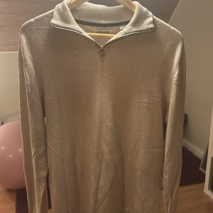 Beige tröja med dragkedja från Jack & Jones - Säljer en stilren beige tröja från Jack & Jones med dragkedja vid halsen. Tröjan har långa ärmar och en mjuk känsla, perfekt för kyligare dagar. Passar bra till både jeans och chinos.