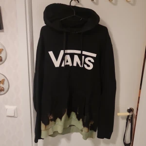 Svart hoodie från Vans - Säljer en svart hoodie från Vans med stort vitt logotryck på framsidan. Tröjan har en unik design med en blekt effekt längst ner. Perfekt för en avslappnad stil.