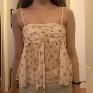 Blommig ärmlös topp med knytning - Söt ljusrosa/rosa-beige ärmlös topp med blommigt mönster och knyt framtill. Använd fåtal gånger, men inga tecken på användning. 