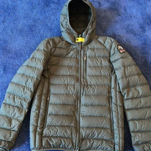 Grön dunjacka från Parajumpers - Säljer en grön dunjacka från Parajumpers med huva och dragkedja. Jackan har en patch på ärmen och är superlätt. Perfekt för kyliga dagar. 🧥