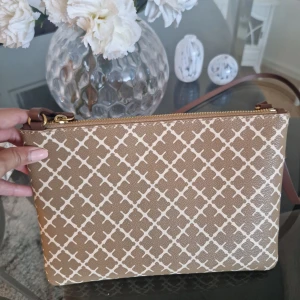 By Malene Birger Beige Väska - Snygg beige axelväska med vitt geometriskt mönster och dragkedja upptill. Perfekt för att bära dina nödvändigheter med stil. Justerbar rem för bekväm passform. Nypris: 899kr. Mått: 25,5 x 18 cm.