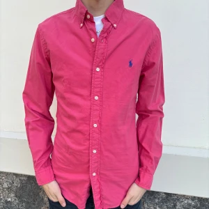 Polo Ralph Lauren skjorta - Säljer en stilren rosa skjorta från Ralph Lauren i slim fit. Skjortan har långa ärmar och knappar framtill samt en broderad logotyp på bröstet. Perfekt för en snygg och avslappnad look.