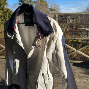 Vit jacka  - Säljer en stilren vit jacka  med marinblå krage och detaljer. Jackan har dragkedja och ribbade muddar vid ärmslut och nederkant. Perfekt för vår och höst!