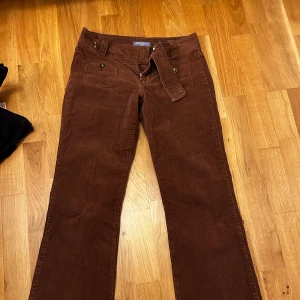Bruna manchesterbyxor lågmidjade bootcut  - Snygga bruna manchesterbyxor  med låg midja och bootcut-stil. Byxorna har knappar och dragkedja framtill samt praktiska fickor. Men en knappt har åkt av men det märks inte av och det är enkelt att fixa en ny