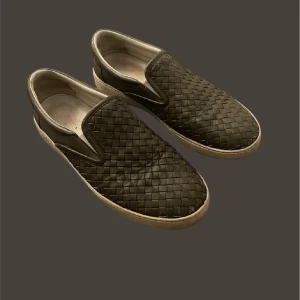 Bottega venetta slip-ons - Snygga svarta loafers med ett unikt flätat mönster. De har en bekväm slip-on design och en vit sula som ger en stilren kontrast. Perfekta för en avslappnad men ändå elegant look.