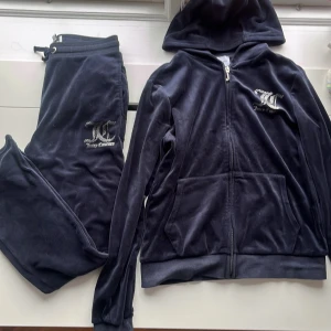 Marinblått set från Juicy Couture - Säljer ett marinblått set från Juicy Couture med byxor och huvtröja. Byxorna har en bekväm passform i midjan och tröjan har dragkedja och huva. Båda delarna har Juicy Couture-loggan i strassdetaljer. Frakt ingår inte i priset!