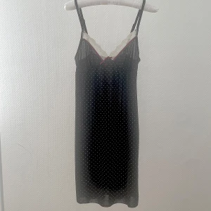 Nattlinne från Lindex - Säljer en svart prickig nattlinne från Lindex med spetsdetaljer och en liten rosett framtill. Passar storlek 36 och 38. Väldigt skön att ha den på sig!