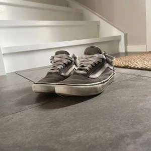 Grå sneakers från Vans - Säljer ett par klassiska grå sneakers från Vans med vit sula och snörning. Skorna har den ikoniska sidostripen i vitt och är perfekta för en avslappnad stil.