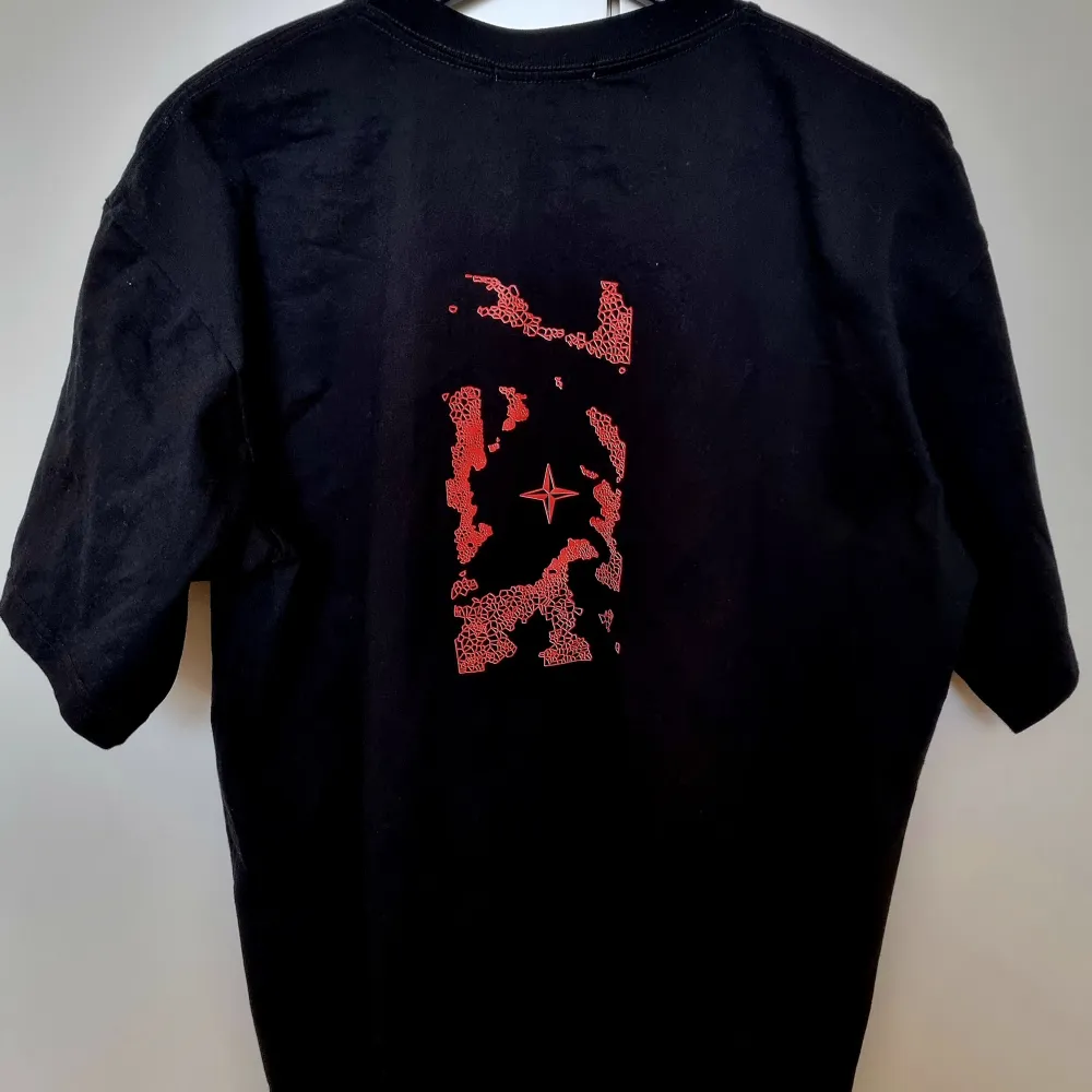 Snygg svart t-shirt från Stone Island med röd logga på bröstet och ett coolt rött mönster på ryggen. Perfekt för en stilren look.. T-paidat.