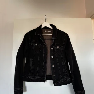 Svart jeansjacka  - Säljer en klassisk svart jeansjacka  med knappar framtill och två bröstfickor.