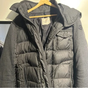 Moncler Jacka Ryan  - Säljer en sällsynt och snygg grå dunjacka från Moncler med avtagbar huva och knappar. Jackan har en quiltad design och flera praktiska drag. Jackan är i väldigt bra skick, skriv vid funderingar😄Storlek 3/Medium