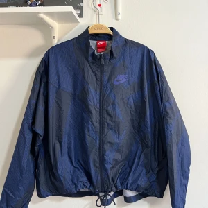 Vintage Nike Windbreaker - Säljer en Vintage Nike windbreaker i stilren svart färg med mörkblått mönster i storlek M. Perfekt för vår, sommar och höst – lätt, vindtät och med justerbar passform tack vare snörning i nederkant!  ✔ Märke: Nike ✔ Färg: Svart med mörkblått mönster – stilren och lätt att matcha ✔ Storlek: M (passar även S för oversized look) ✔ Material: Nylon/polyester – vindtätt och lättvikt ✔ Passform: Regular fit, kan justeras för mer slim eller relaxed look ✔ Skick: A (Utmärkt skick, inga skador eller fläck