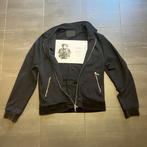 Limitato  - Snygg svart bomberjacka med dragkedjor framtill och en cool bild på ryggen. Jackan har långa ärmar och ribbade muddar vid ärmslut och nederkant. Perfekt för en stilren look.