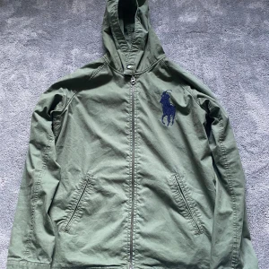 Ralph Lauren Jacka - Tja! Säljer en grön jacka från Polo Ralph Lauren som är perfekt för våren. Jackan är i storlek 14-16 vilket motsvarar ungefär S men passar även xs. Jackan är i 9/10 skick då det ändå tecknet av användning är ett litet märke från att dragkedjan fastnat i jackan (se bild 3). Det lilla märket är trots det inte något man ser. Hör av er vid minsta lilla fundering.