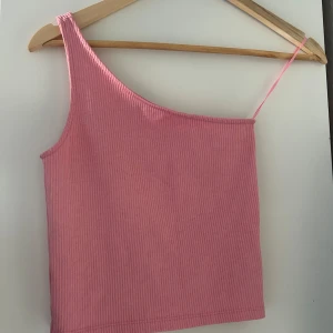 Rosa ribbad oneshoulder topp från Gina Tricot - Säljer en söt rosa ribbad oneshoulder topp från Gina Tricot. Perfekt för varma dagar eller en utekväll. Den har en smal axelrem och en asymmetrisk design som ger en trendig look.