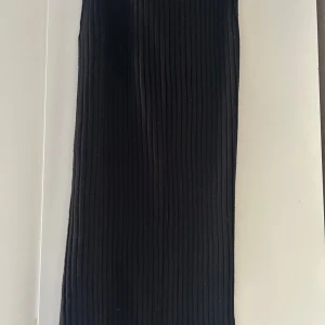 Svart ribbad kjol från Lindex - Snygg svart ribbad kjol från Lindex i storlek XS. Perfekt för en stilren look med sin enkla design och bekväma passform. Kjolen är i ett stretchigt material som gör den lätt att bära.