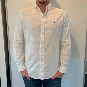 Vit skjorta från Ralph Lauren - Säljer en stilren vit skjorta från Ralph Lauren i slim fit. Skjortan har långa ärmar och klassiska knappar framtill. Perfekt för en elegant look. Hör av er vid minsta fundering!