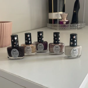 Nagellack från Ciaté - Fem olika nagellack från Ciaté med stjärnmönstrade lock. Färgerna inkluderar mörklila, guldglittrig, ljusrosa, rödglittrig och ljusgrå. Perfekt för att variera din nagelstil med både glittriga och matta alternativ.