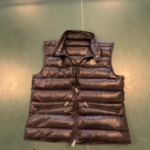 Svart dunväst från Moncler - Snygg svart dunväst från Moncler. Dragkedjan är trasig så du kommer behöva dra på dig västen över huvudet. Så du kommer inte kunna öppna dragkedjan då jag sytt igen den. Men de gör ingenting. Nypris 8499kr. De är storlek 3 vilket är samma som M. Pris diskuterbart