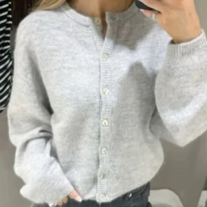 Grå kofta med knappar - Säljer en mysig grå kofta med knappar framtill. Koftan har en rund halsringning och långa armar. Väldigt modern och super fin kofta!!