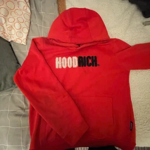 Röd hoodie från Hoodrich - Säljer en cool röd hoodie från Hoodrich med stor logga i vitt och svart på bröstet. Tröjan har en klassisk känguruficka och en bekväm huva. Perfekt för en avslappnad stil. Passar ungdomar i åldern 12-13 år.
