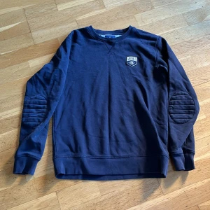 Mörkblå tröja från GANT - En rundhalsad, mörkblå tröja från GANT. Den är tillverkad av bomull och har en väldigt avslappnad look. 