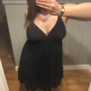Svart klänning med v-ringning - Säljer en elegant svart klänning med v-ringning och smala axelband. Klänningen har en fin passform, med dess detaljer i ryggen och är perfekt för festliga tillfällen. Den har en kort längd och en stilren design.
