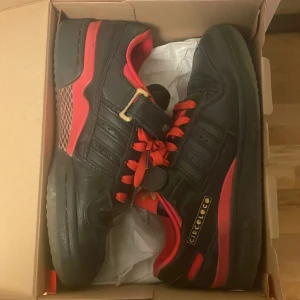 Svarta och röda sneakers från Adidas - Snygga svarta sneakers med röda detaljer från Adidas. Skorna har en klassisk design med snörning och kardborreband för extra stöd. Perfekta för en sportig look med Circoloco-logga på sidan. Pris kan diskuteras.