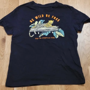 Svart t-shirt med leopardtryck - Säljer en svart t-shirt med ett coolt leopardtryck och texten 'Be Wild Be Free'. Perfekt för dig som älskar djur och natur. T-shirten har korta ärmar och är gjord i bomull för en skön känsla. Passar perfekt till vardagsäventyr! Storlek 158/164 men passar även XS/S.