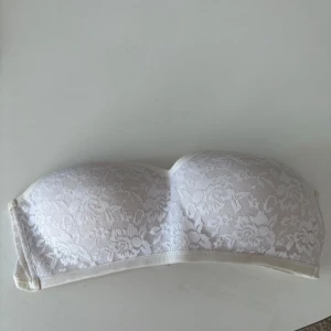 Vit spets tubtopp från Gina Tricot - Säljer en elegant vit tubtopp från Gina Tricot med vacker spetsdetalj. Storlek L