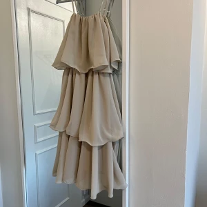 Beige volangklänning - Beige klänning med flera lager volanger och smala axelband. Använd två gånger av tidigare köparen, bilder tagna från henne. Säljer då den inte passade!