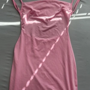 Rosa axelbandslös klänning - Säljer en snygg rosa axelbandslös klänning med öppen rygg. Perfekt för sommarens fester. Klänningen har en figurnära passform och är gjord i ett mjukt material.