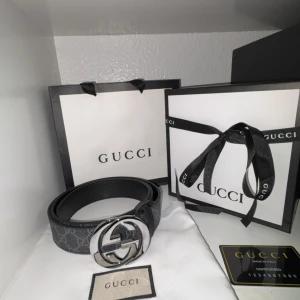 Svart bälte från Gucci - Snyggt svart bälte från Gucci med ett stort, runt spänne i silver. Bältet har ett diskret mönster och är tillverkat i skinn. Perfekt för att ge en lyxig touch till din outfit.
