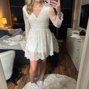 Vit spetsklänning med öppen rygg - Säljer en vacker vit spetsklänning med långärmade ärmar och en elegant öppen rygg. Klänningen har en v-ringad hals och är perfekt för speciella tillfällen. Den är tillverkad i ett fint spetsmaterial. Går att dra upp dragkedjan ytterligare, men behövs assistans