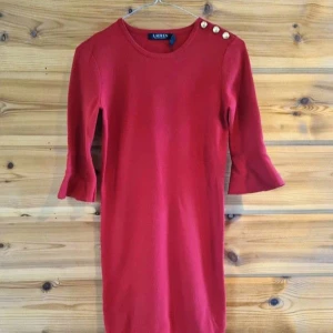 Röd klänning från Ralph Lauren - Snygg röd klänning från Ralph Lauren med trekvartsärmar och dekorativa guldknappar på axeln. Perfekt för en elegant look. Klänningen har en klassisk passform och är tillverkad i ett mjukt material❤️