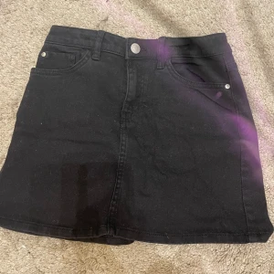 Svart jeanskjol - Snygg svart jeanskjol med klassisk femficksdesign och knappstängning fram. Perfekt för en stilren look.