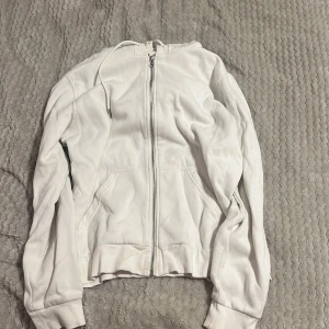 Vit hoodie med dragkedja - Säljer en hoodie med dragkedja och långa ärmar. Hoodien har praktiska fickor framtill och ribbade muddar vid ärmslut och nederkant. Perfekt för en stilren look. Har tyvärr fläckar som knappast syns, vet ej om det går att tvätta bort. Har använd lite. 63% bomull, 37% polyester. Hör av dig för eventuella frågor 🌸kolla gärna in mina andra annonser!⤵️✨