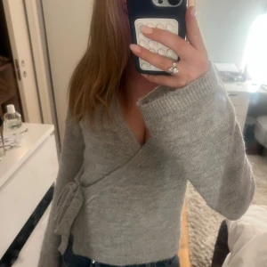 Grå omlottkofta från Gina Tricot - Säljer en mysig grå omlottkofta från Gina Tricot i premiumkvalitet. Koftan har långa ärmar och knytning i sidan, perfekt till våren ❤️