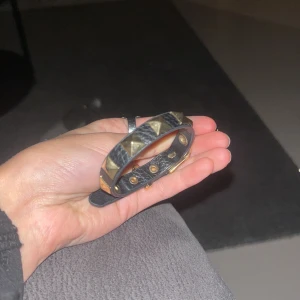 Svart armband med nitar - Snyggt svart armband med guldiga nitar. Armbandet har en justerbar rem och en cool design som passar perfekt för att ge en edgy touch till din outfit. Använd 2 gånger så inga skador. 