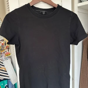 Svart t-shirt från COS - Säljer en klassisk svart t-shirt från COS i storlek XS. Den har en rund halsringning och korta ärmar, perfekt för en stilren look. Tillverkad i mjukt material för bekväm passform.