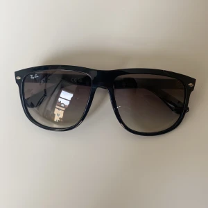 Svarta Ray-Ban Boyfriend solglasögon - Snygga svarta solglasögon från Ray-Ban med klassisk design. De har en robust båge och mörka linser som ger ett stilrent intryck. Perfekta för soliga dagar. Levereras med ett brunt fodral och putsduk. Knappt använda.